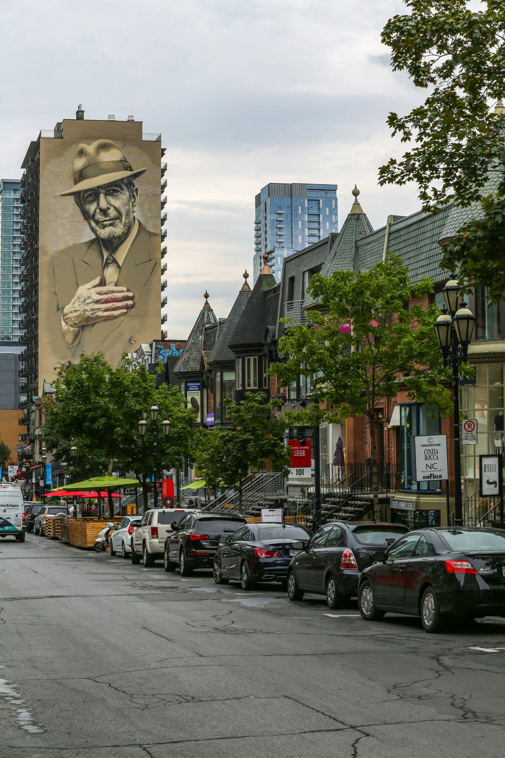 Cars park on a street in Montreal overlooked by a Leonard Cohen mural.